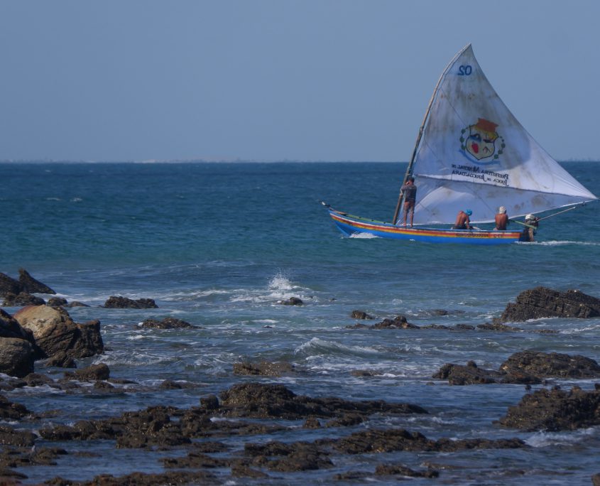 Pescadores voltando para a praia em uma jangada, vela com o brasão de Jijoca de Jericoacoara