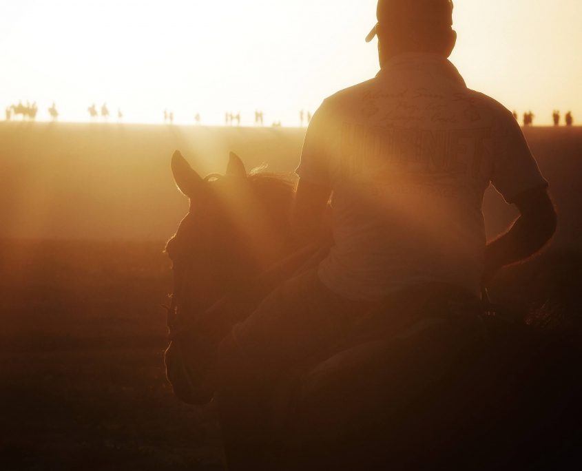 Homem passeando à cavalo na próximo a duna do pôr do sol